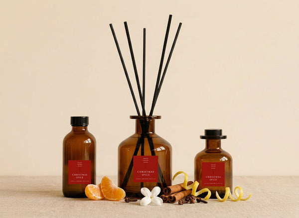 Christmas Spice reed diffusers in three sizes, amber glass with deep red labels and black reeds, styled with satsuma segments, cinnamon sticks, cloves and citrus peel