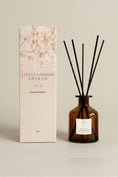 Load image into Gallery viewer, Festive Cranberry 250ml reed diffuser, large amber bottle with black reeds, beside its cream floral-print Little London Gifts Co gift box