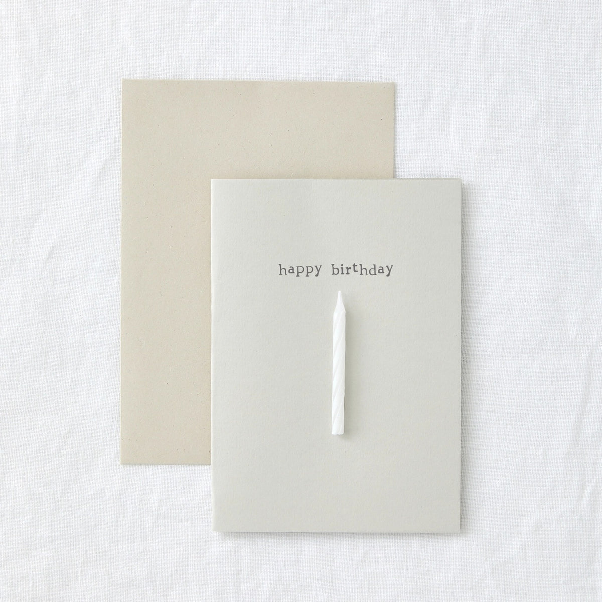 Birthday card in cream paper reading 'happy birthday', with a die cut slot holding a slim candle
