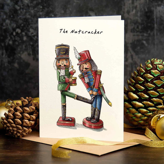 Christmas card titled 'The Nutcracker', with two illustrated nutcracker soldiers, standing among pine cones and gold baubles