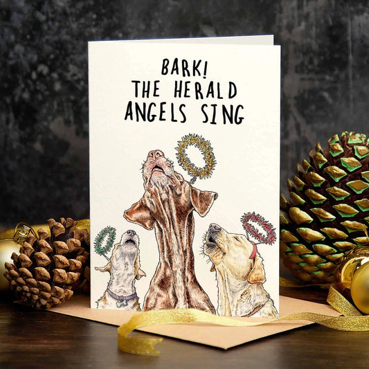 Christmas card reading 'Bark! The herald angels sing', with three dogs in angel wreaths, standing among pine cones and gold baubles