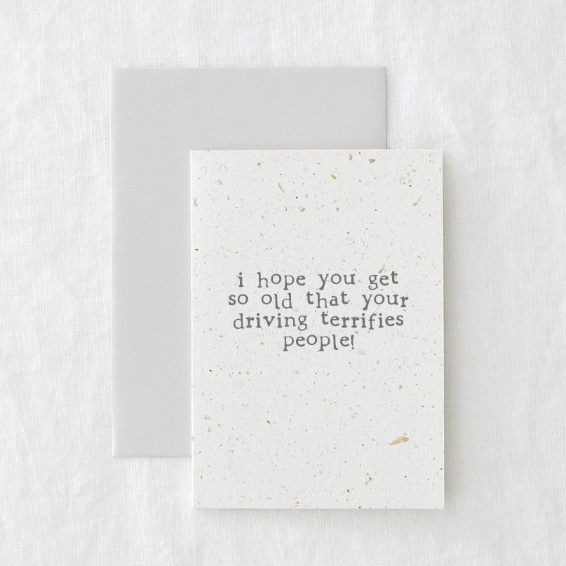 Birthday card in speckled cream paper reading 'I hope you get so old that your driving terrifies people', shown with its envelope