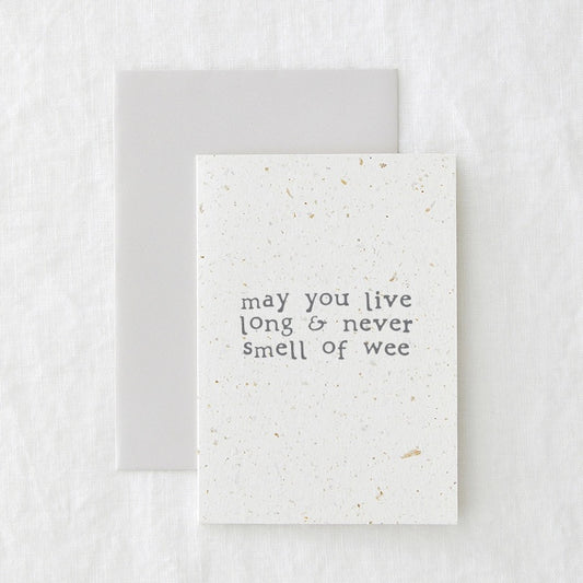 Birthday card in speckled cream paper reading 'may you live long and never smell of wee', shown with its envelope