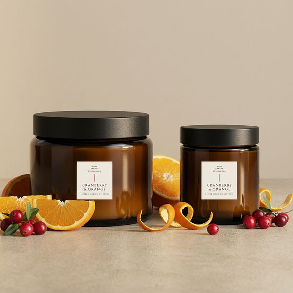 Cranberry & Orange candles in two sizes, amber glass jars styled with orange slices and cranberries