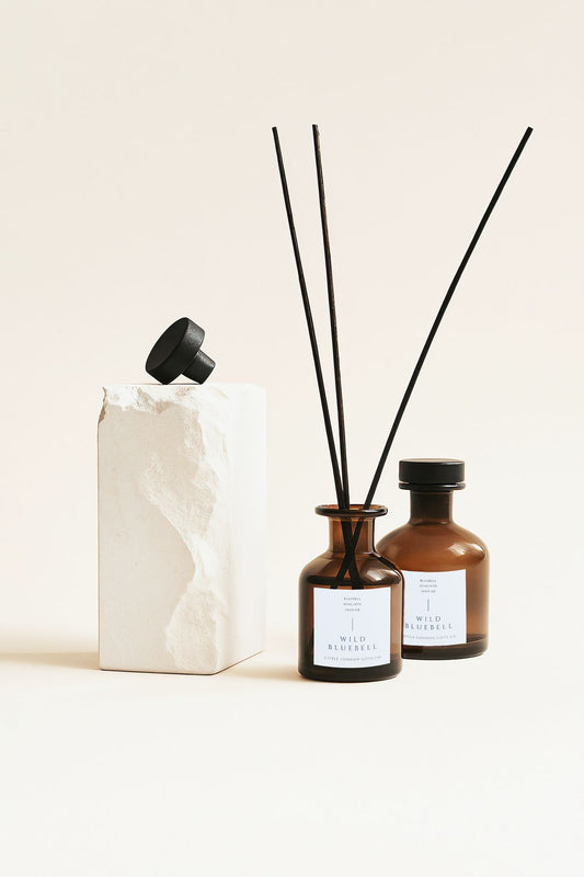 Two English Bluebell reed diffusers with black reeds beside a textured white sculpture