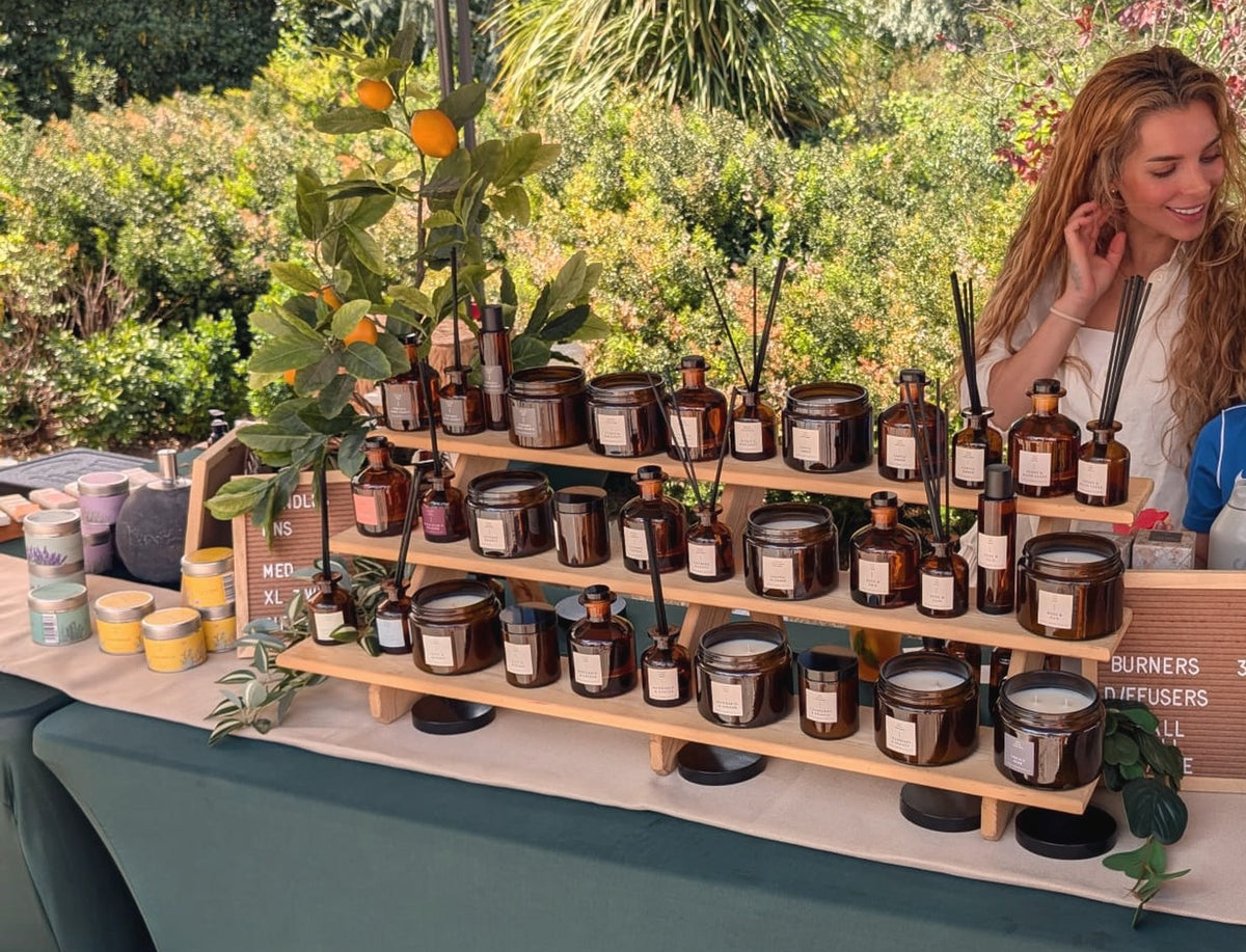 Helia Sinclair smiling behind her Little London Gifts Co market stall of candles and reed diffusers