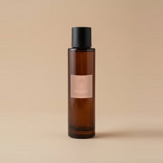 Bouquet room spray 100ml, amber glass bottle with a matte black cap and blush label, on a warm beige backdrop