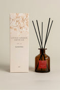 Load image into Gallery viewer, Christmas Spice 250ml reed diffuser in amber glass with black reeds, beside its printed Little London Gifts Co gift box
