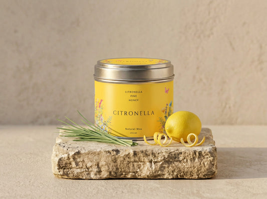 Citronella candle tin in brushed silver with a yellow wildflower label, styled with lemongrass, a lemon and curled citrus peel