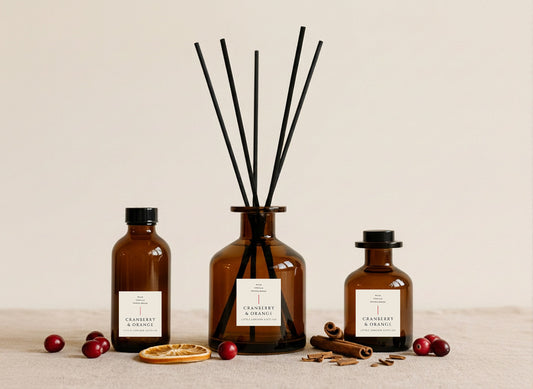 Cranberry & Orange reed diffusers in three sizes, amber glass with black reeds, styled with fresh cranberries, dried orange and cinnamon sticks