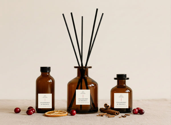 Cranberry & Orange reed diffusers in three sizes, amber glass with black reeds, styled with fresh cranberries, dried orange and cinnamon sticks