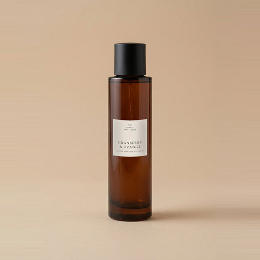 Cranberry & Orange room spray 100ml, amber glass bottle with a matte black cap and cream label, on a warm beige backdrop