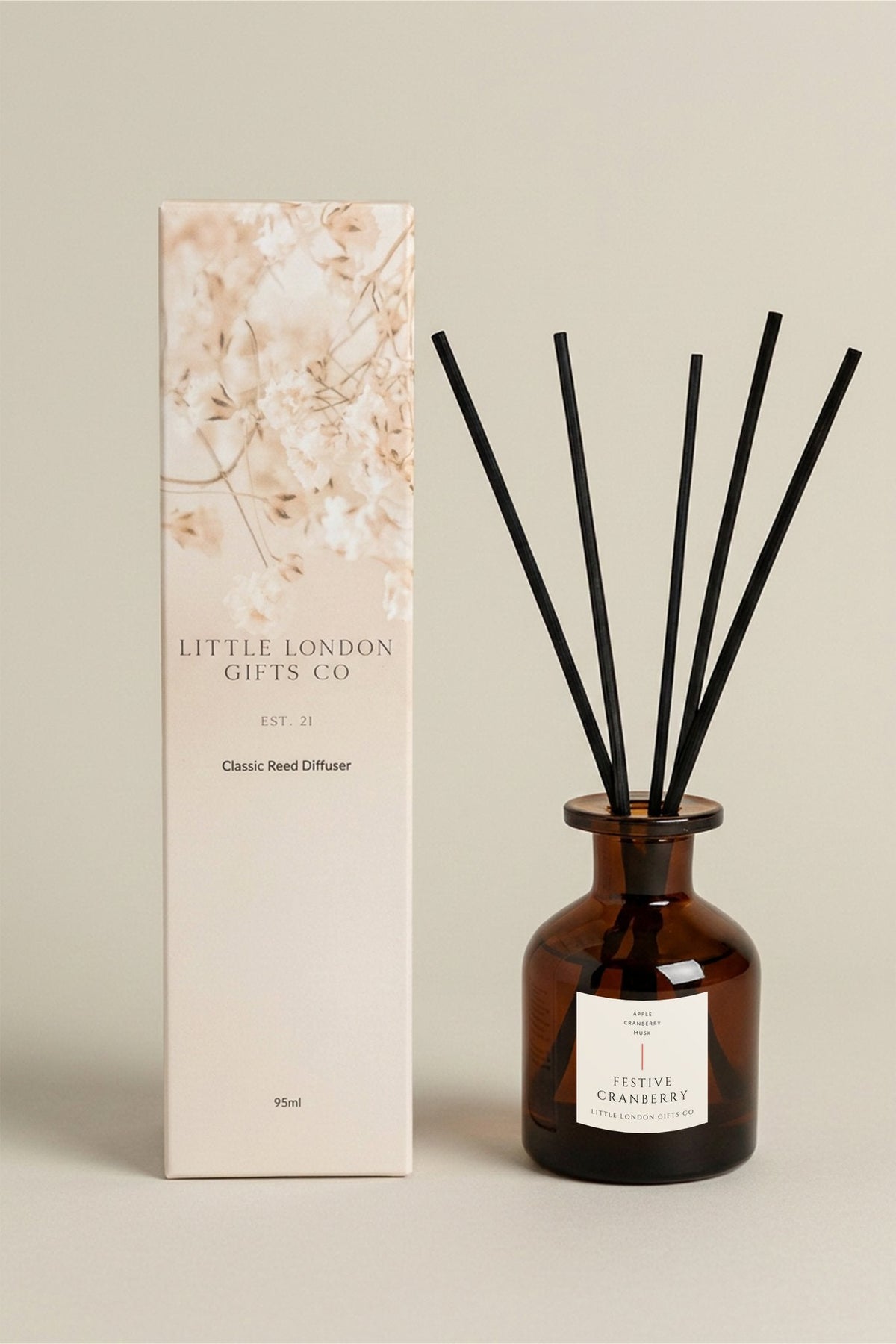 Festive Cranberry 95ml reed diffuser in amber glass with black reeds, beside its cream floral-print Little London Gifts Co gift box