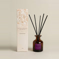Load image into Gallery viewer, Plum & Rhubarb 95ml reed diffuser in amber glass with black reeds beside its cream floral-print gift box
