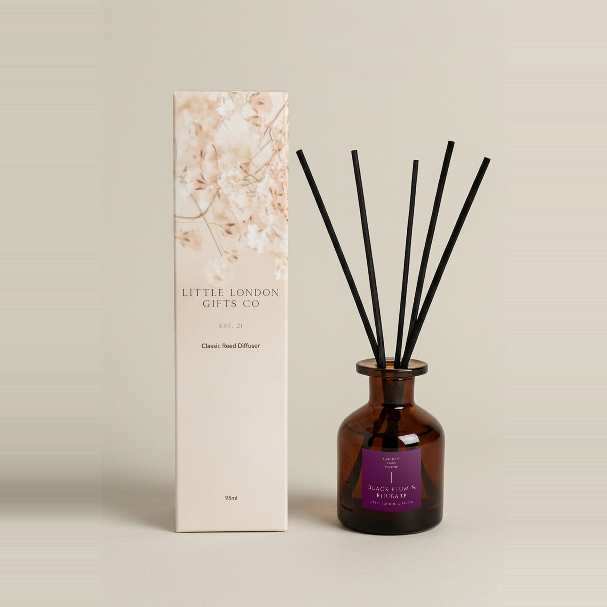 Plum & Rhubarb 95ml reed diffuser in amber glass with black reeds beside its cream floral-print gift box