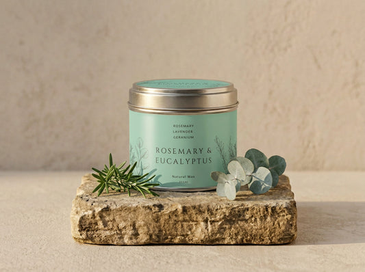 Rosemary & Eucalyptus candle tin in brushed silver with a pale green label, styled with fresh rosemary and eucalyptus leaves on stone