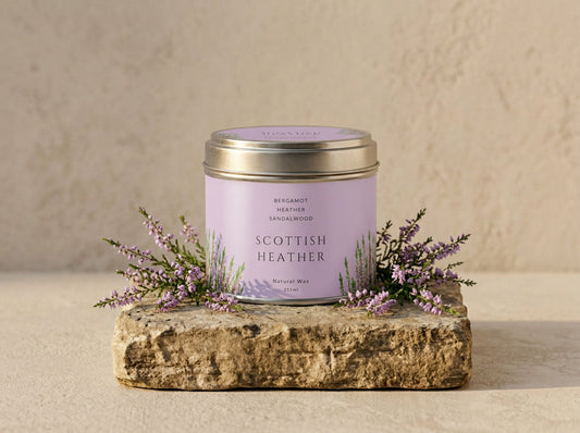 Scottish Heather candle tin in brushed silver with a soft lilac label, styled with sprigs of flowering heather on a stone slab