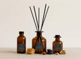 Load image into Gallery viewer, Vintage Dark Honey reed diffusers in three sizes, amber glass with charcoal labels and black reeds, styled with honeycomb, tonka beans and amber resin
