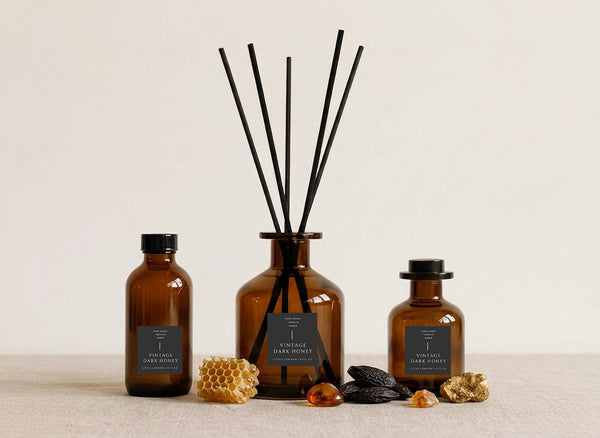 Vintage Dark Honey reed diffusers in three sizes, amber glass with charcoal labels and black reeds, styled with honeycomb, tonka beans and amber resin