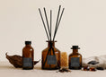 Load image into Gallery viewer, Vintage Dark Honey reed diffusers in three sizes, amber glass with charcoal labels and black reeds, styled with honeycomb, tobacco leaf and amber
