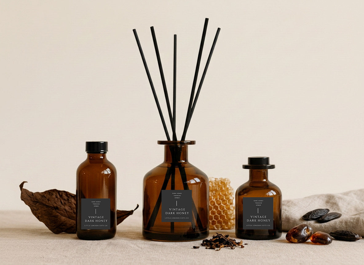 Vintage Dark Honey reed diffusers in three sizes, amber glass with charcoal labels and black reeds, styled with honeycomb, tobacco leaf and amber