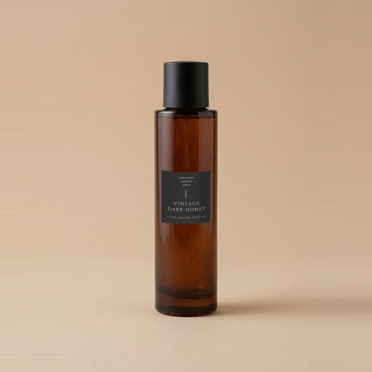 Vintage Dark Honey room spray 100ml, amber glass bottle with a matte black cap and charcoal label, on a warm beige backdrop