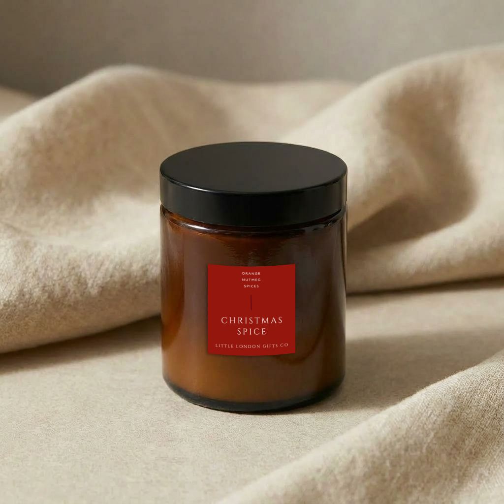 Christmas Spice candle in amber glass with its black lid on, resting on a cream knitted throw
